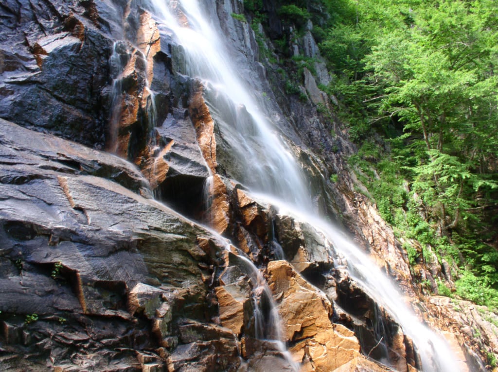 Mist rises where Arethusa Falls spreads across the dark cliff.