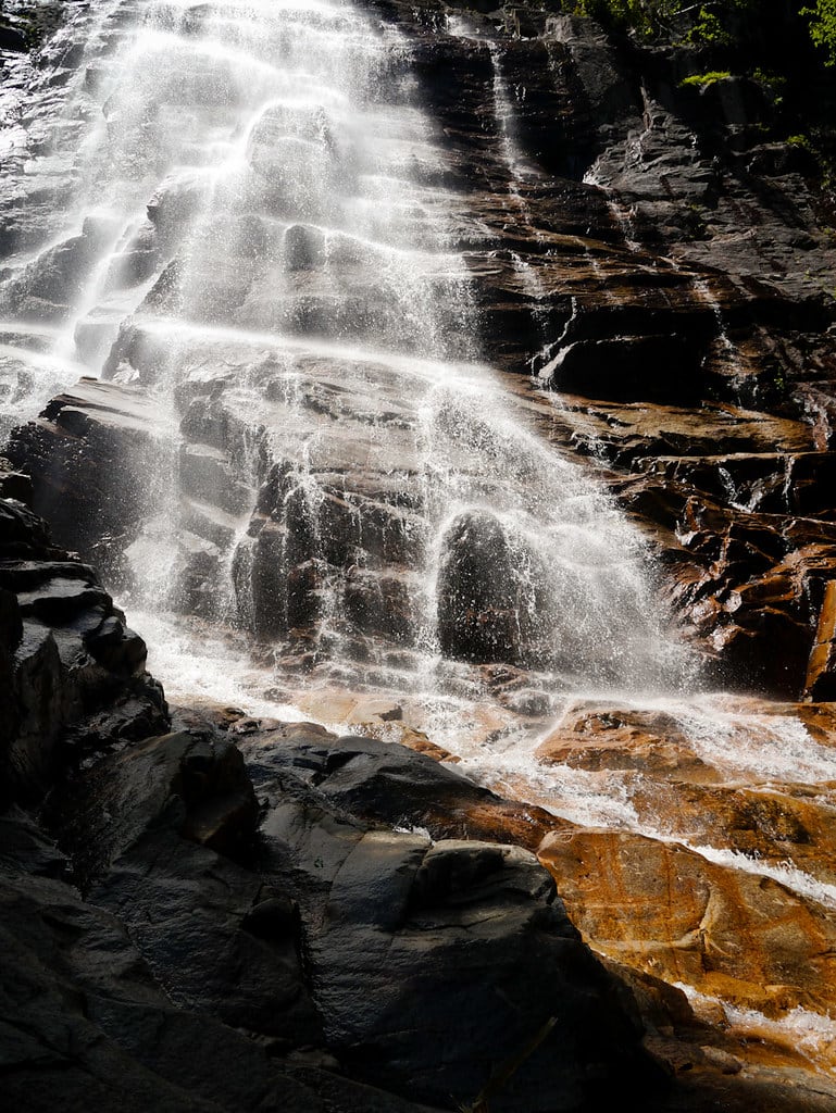 Sun catches the wet rock ledges below Arethusa Falls.
