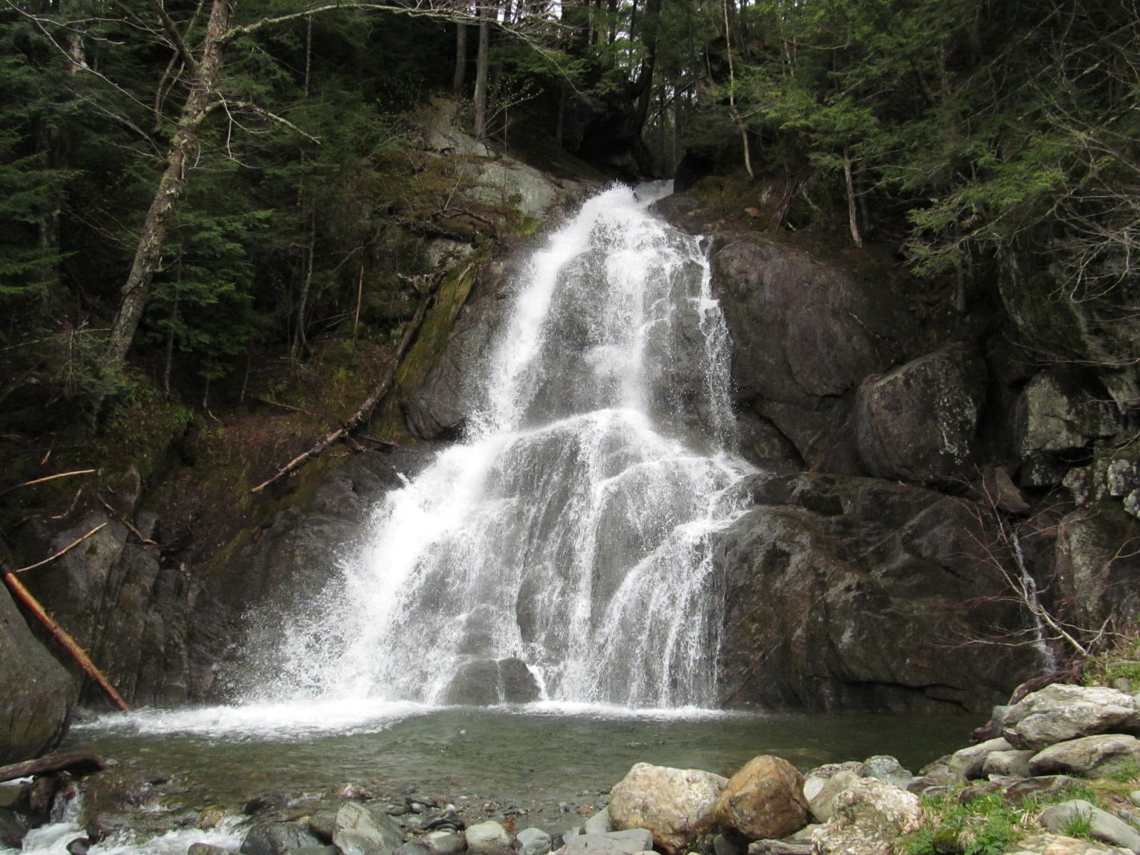 Wide view of Moss Glen Falls in Stowe with boulders and a green pool below the falls.